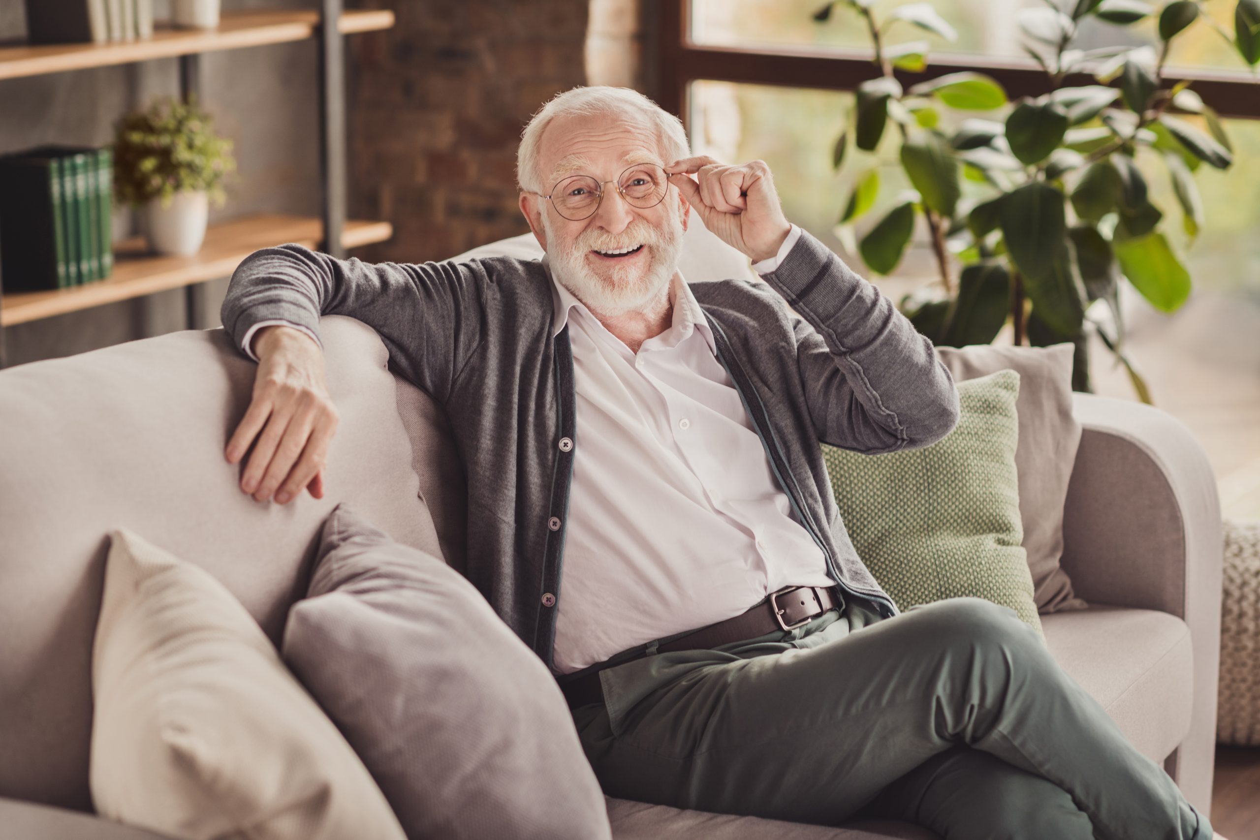 Photo of handsome pensioner wear grey cardigan smiling arm glasses sitting couch indoors house flat